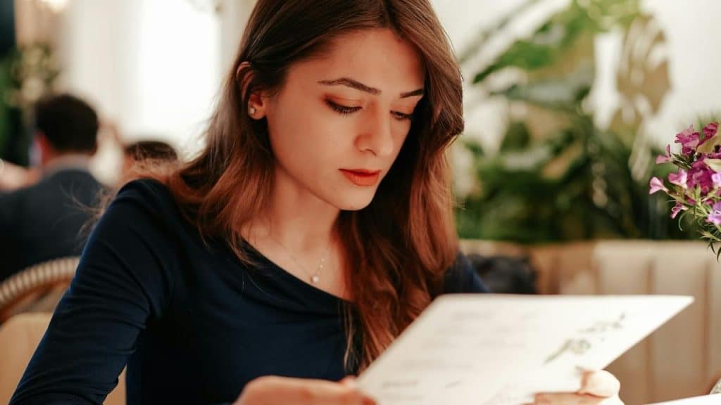 A woman reading a menu while seated at a café table.