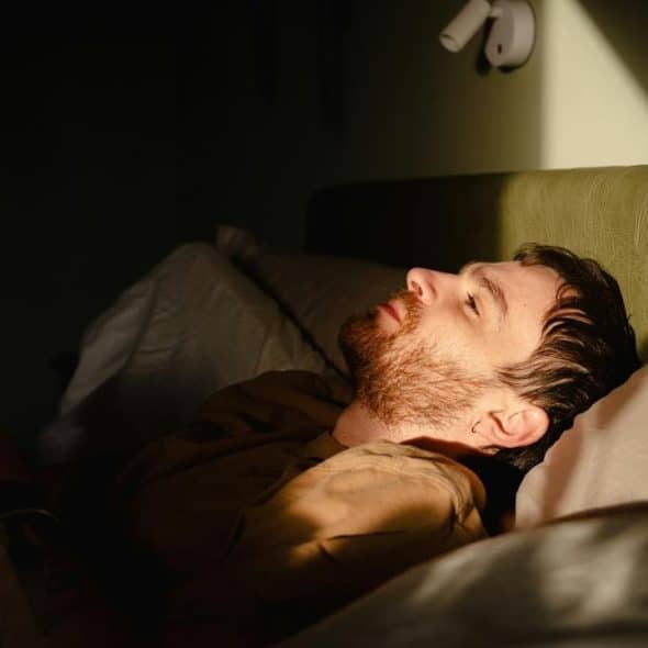 A man lying in bed, holding a book as warm light falls across his face.