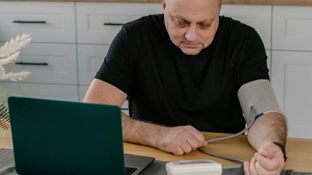 A man sits at a desk with a blood pressure cuff wrapped around his upper arm.