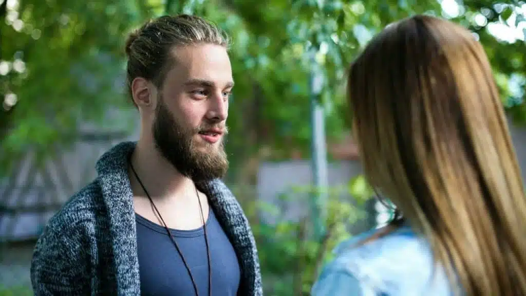 A man with a beard and hair in a bun looks at a woman's back.