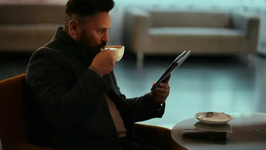 A man drinking coffee while reading a newspaper in a lounge.