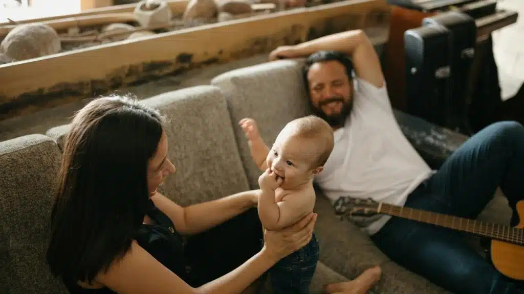 A couple relaxing on a couch with their smiling baby.