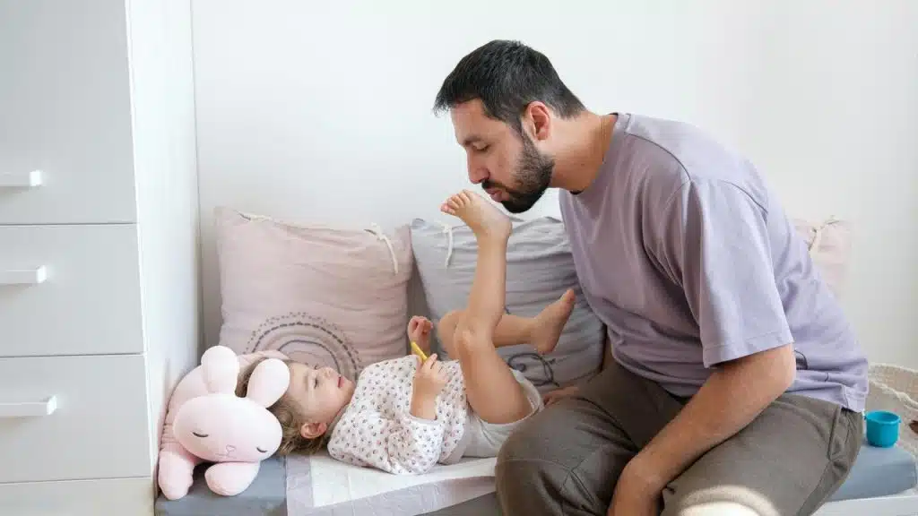 A man playing with a child lying on a bed.