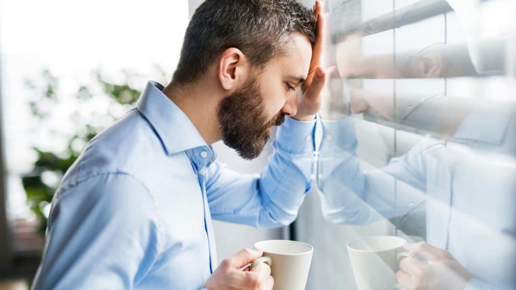A man in a blue shirt leaning his head against a window.
