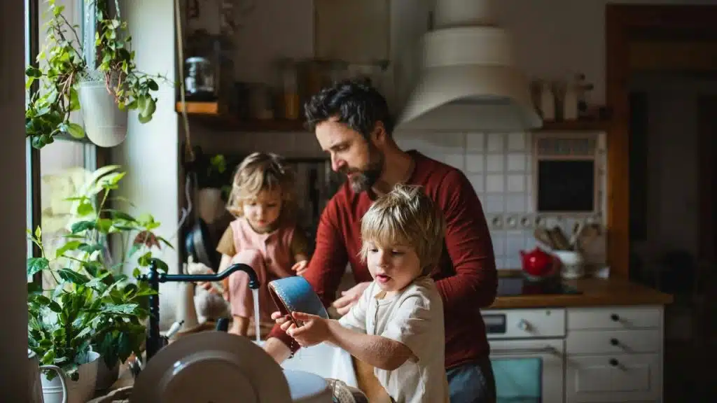 A father and two children washing dishes together in a kitchen.