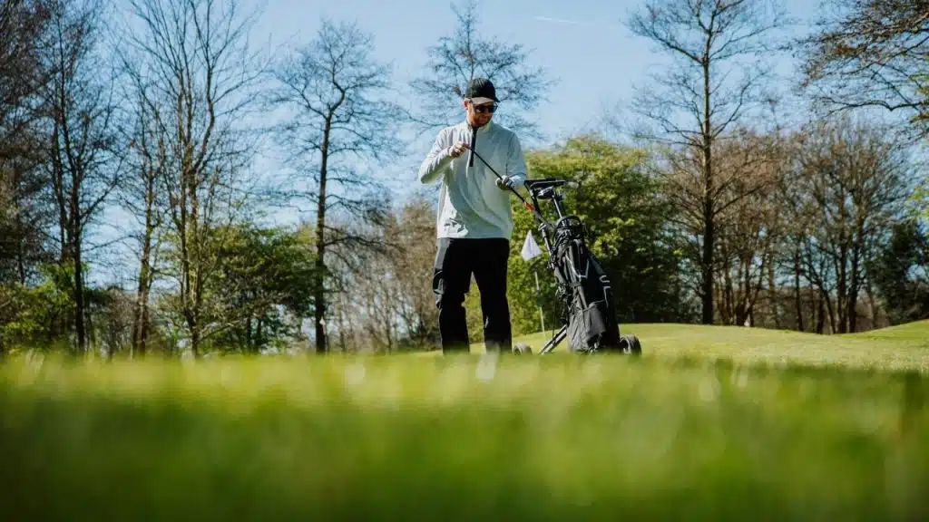 A man standing on a golf course with a golf bag.