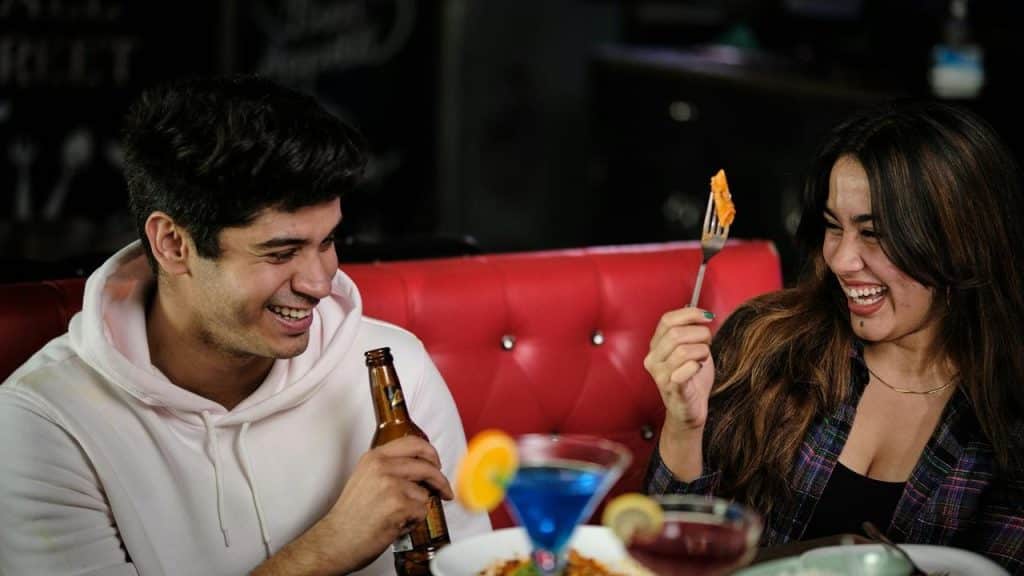 A man and woman laughing together while enjoying drinks and food at a restaurant.