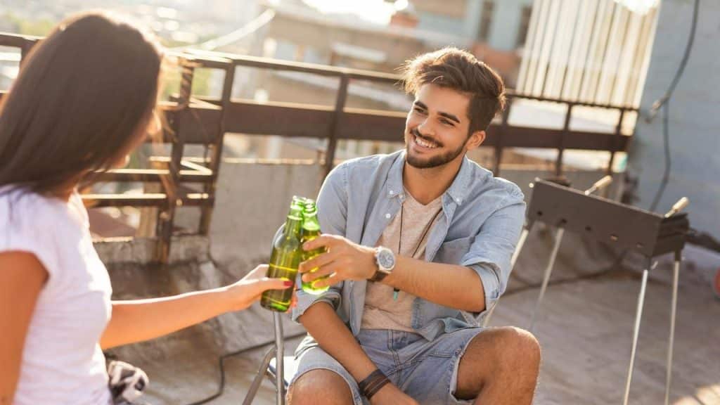 A man and woman clinking beer bottles on a rooftop.