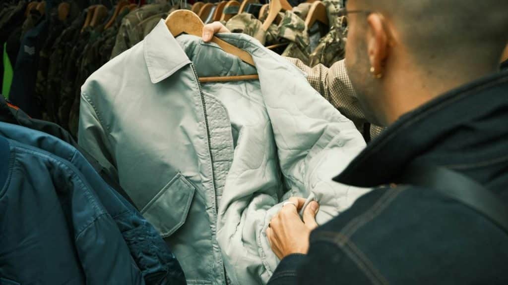 A person examines the lining of a light-colored jacket on a clothing rack.