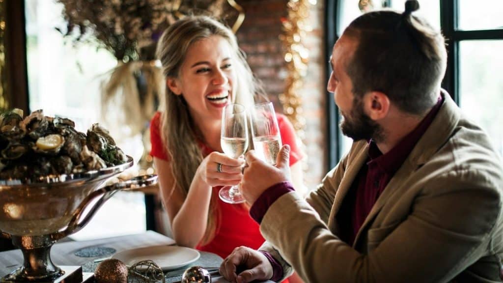 A man and woman laughing while toasting with champagne at a restaurant.