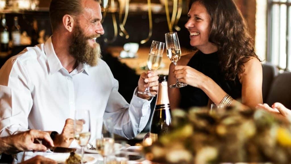 A man and woman smiling while clinking champagne glasses at a restaurant.