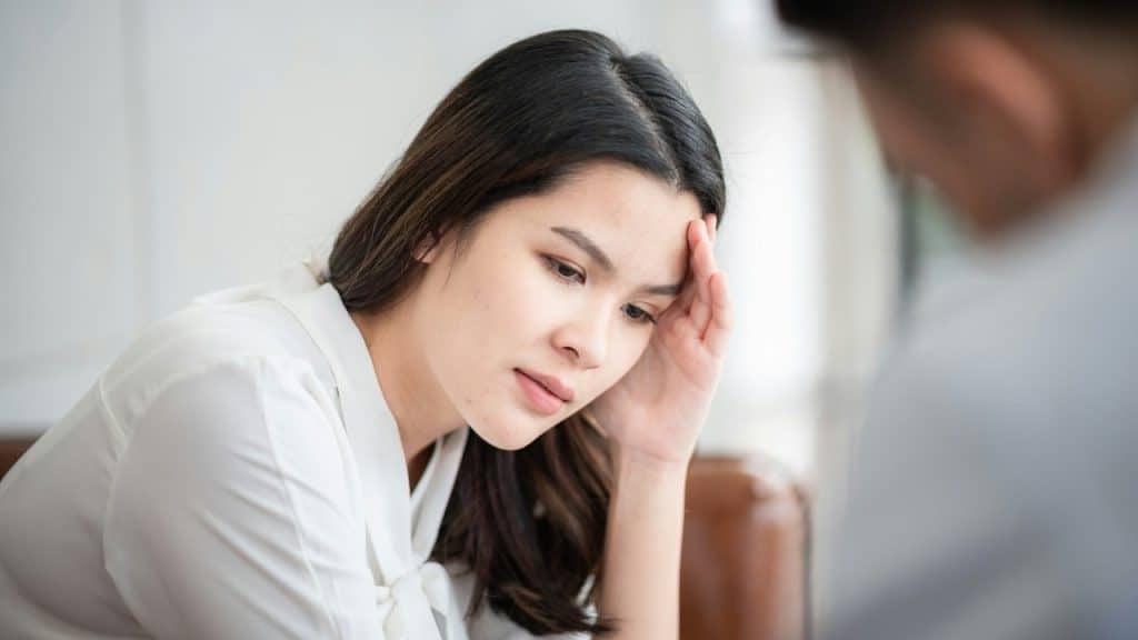 A woman rests her head on her hand with a downward gaze during a conversation.