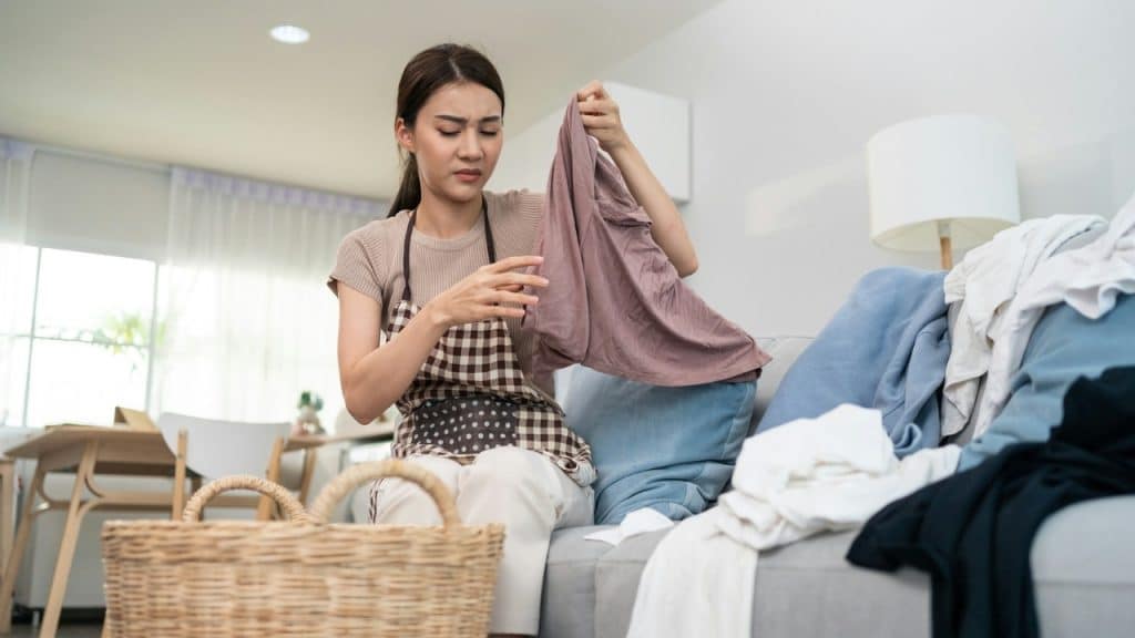 A woman wearing an apron sits on a sofa, looking at a piece of laundry.