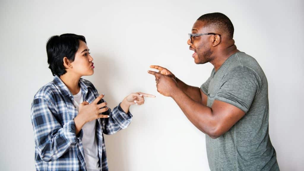 A man and woman gesture intensely toward each other with open mouths and expressive faces.