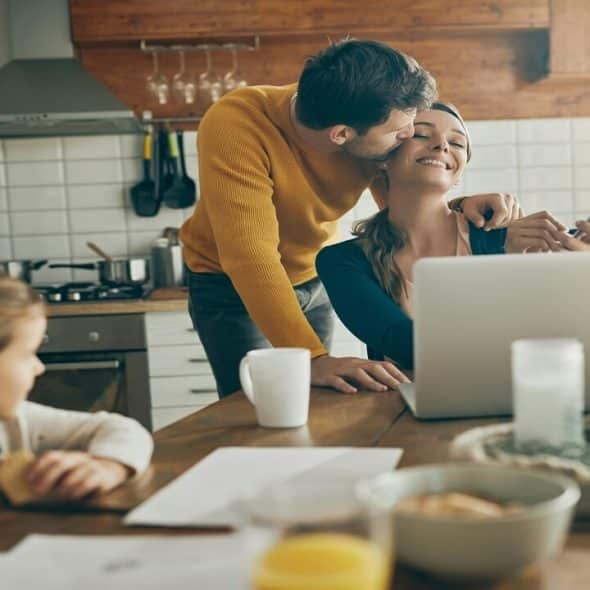 A man kissing his wife in the kitchen