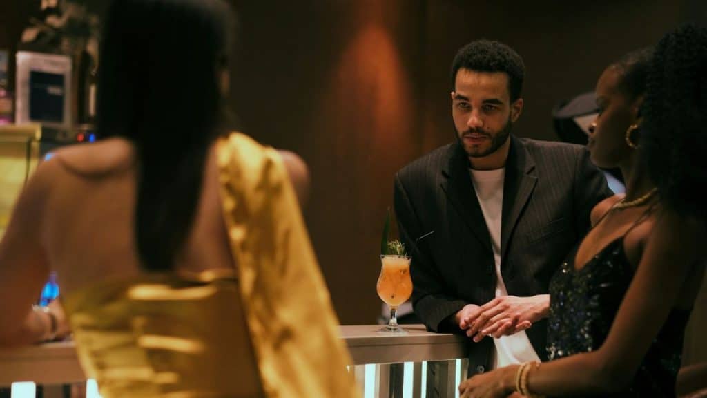 A man in a suit stands at a bar talking to two women near a cocktail.