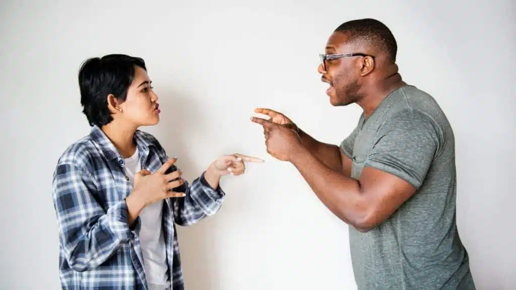 A man and woman stand facing each other while gesturing and speaking with intensity.