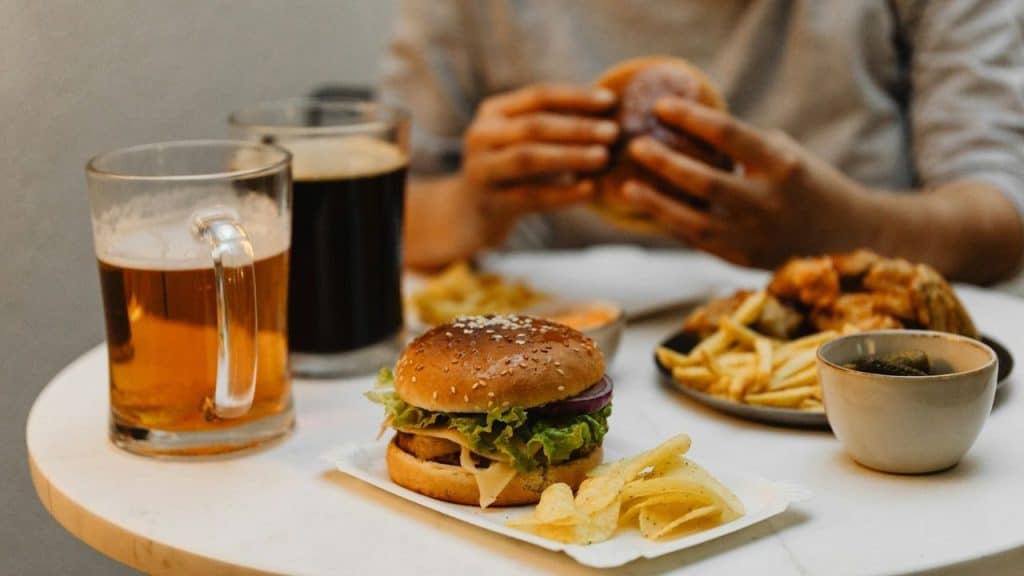 A close-up of a table featuring a burger, fries, and two glasses of dark beer.