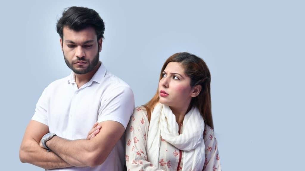A woman in a patterned top stares intently at a man standing with crossed arms.