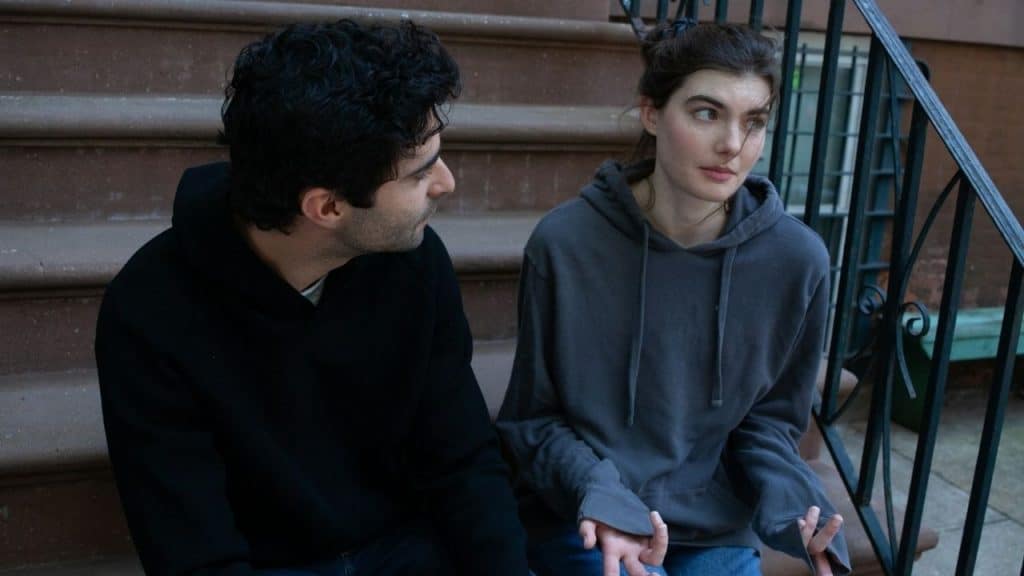 A man and woman wearing hoodies sit together on stone steps and engage in conversation.