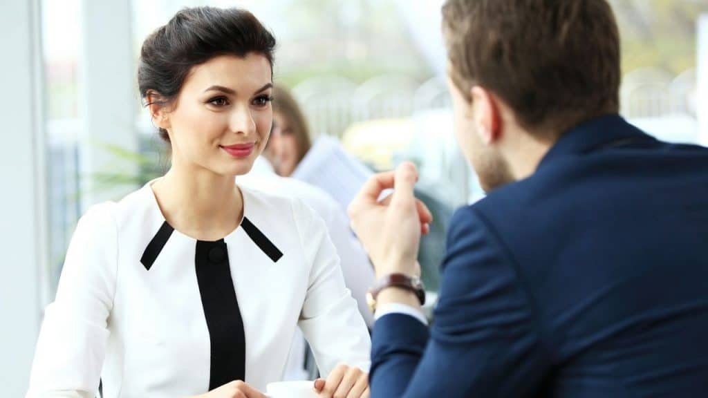 A woman in a white blouse with black trim listens intently to a man in a suit.