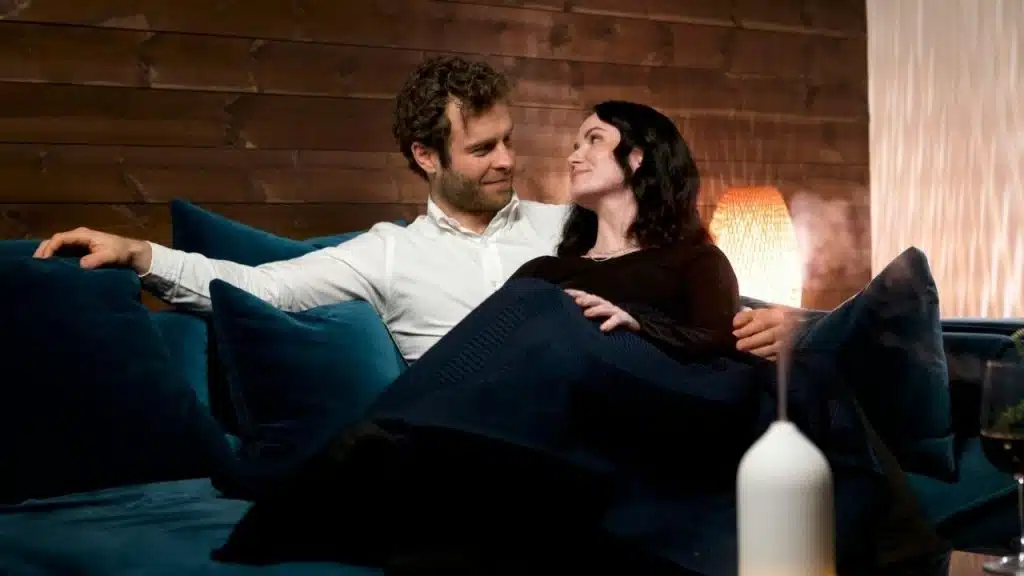A man and woman lounge closely on a blue sofa while sharing direct eye contact.