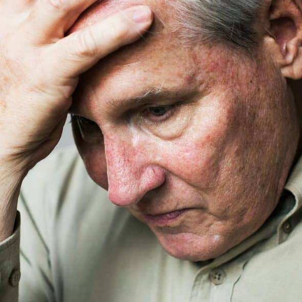 A thoughtful older man resting his hand on his forehead while looking down.