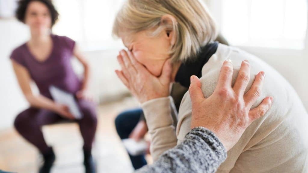 A thoughtful older man resting his hand on his forehead while looking down.