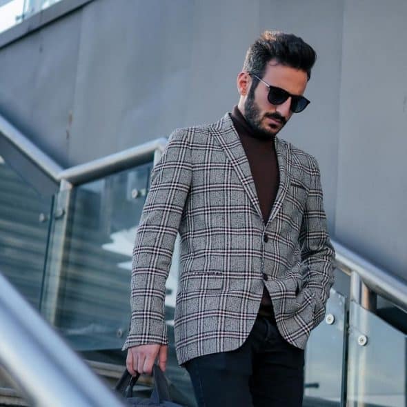 A stylish man wearing sunglasses and a plaid blazer walking down modern outdoor stairs.