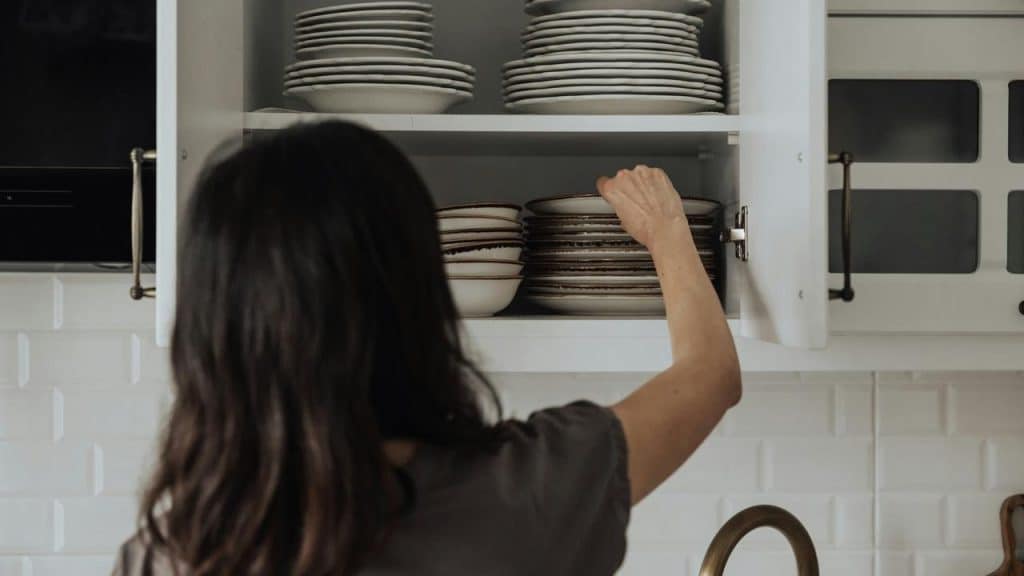 A person reaching into a kitchen cabinet to arrange stacked plates.