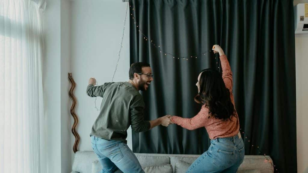 A couple dancing together in a living room decorated with string lights.