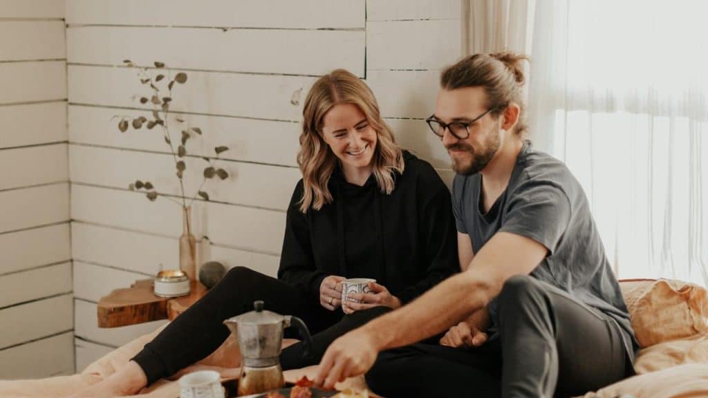 A couple sitting on a bed sharing coffee and a relaxed moment together.