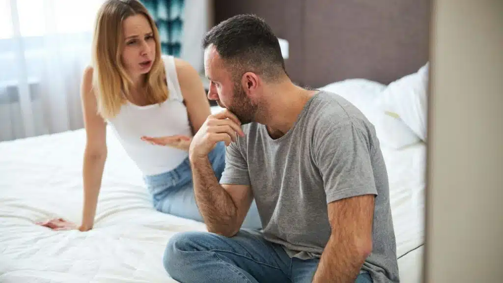 Angry woman arguing with a sad-looking man on a bed.