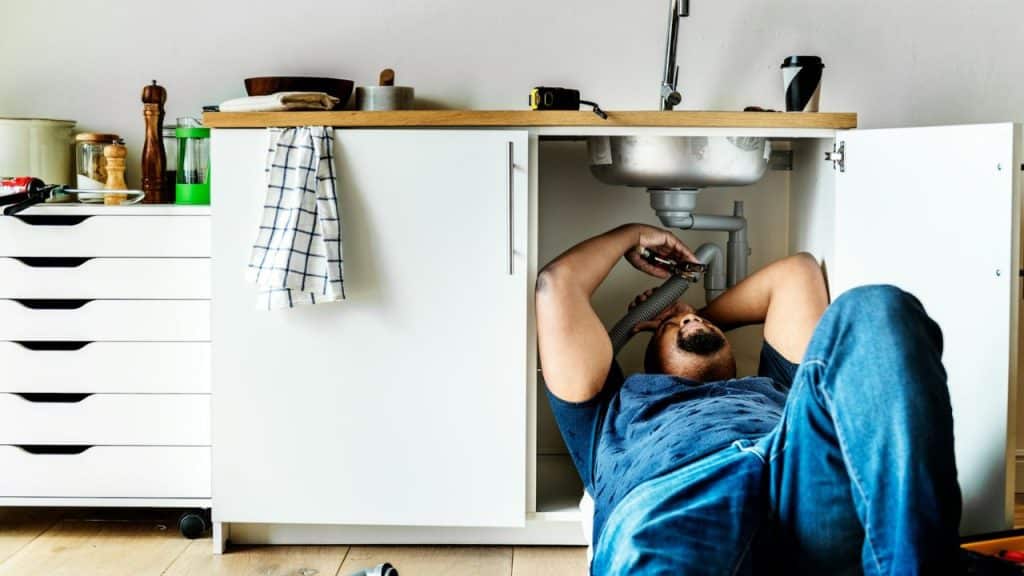 Man lying on his back under a kitchen sink, working on the plumbing.