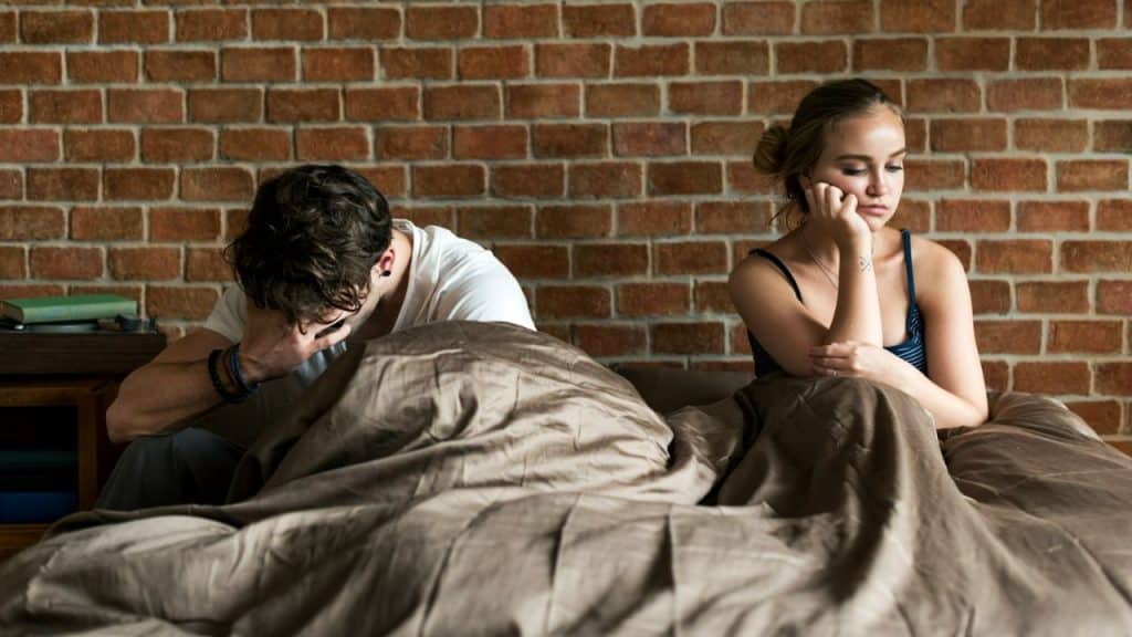 Two people sitting in bed with their backs to each other after an argument.