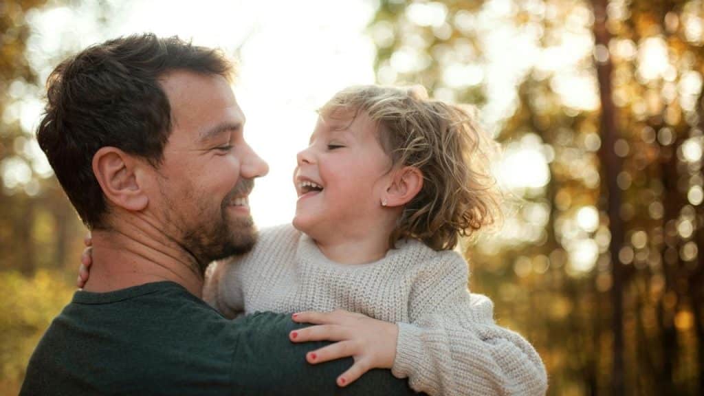 A father holding his laughing child in a sunlit forest.