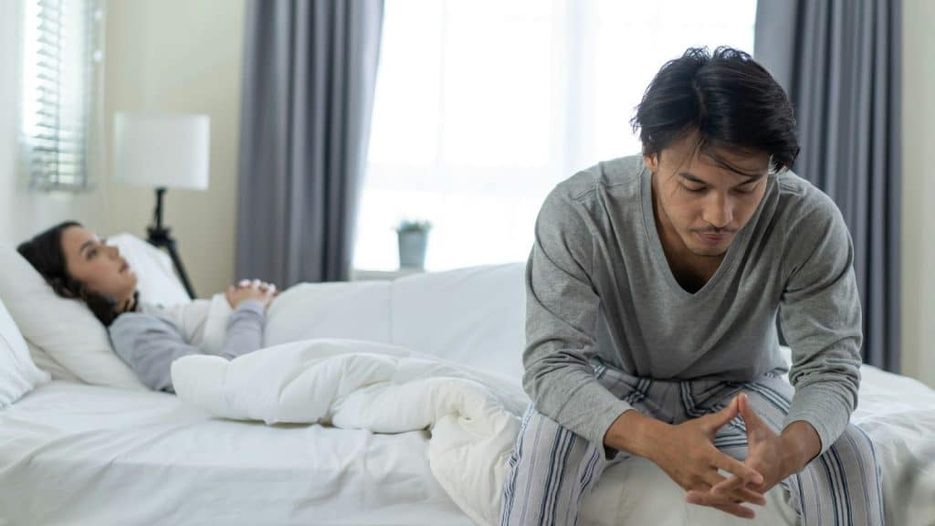 A woman lying on bed and a man sitting at the corner of the bed