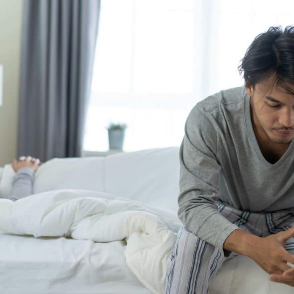A woman lying on bed and a man sitting at the corner of the bed