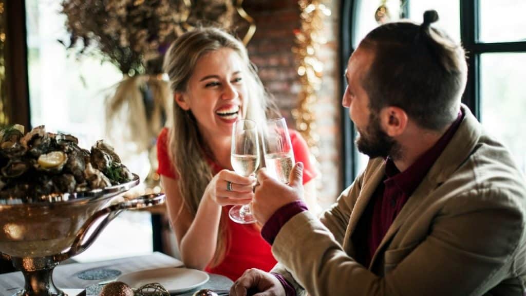 A happy couple toasts with champagne glasses over a plate of oysters in a restaurant.