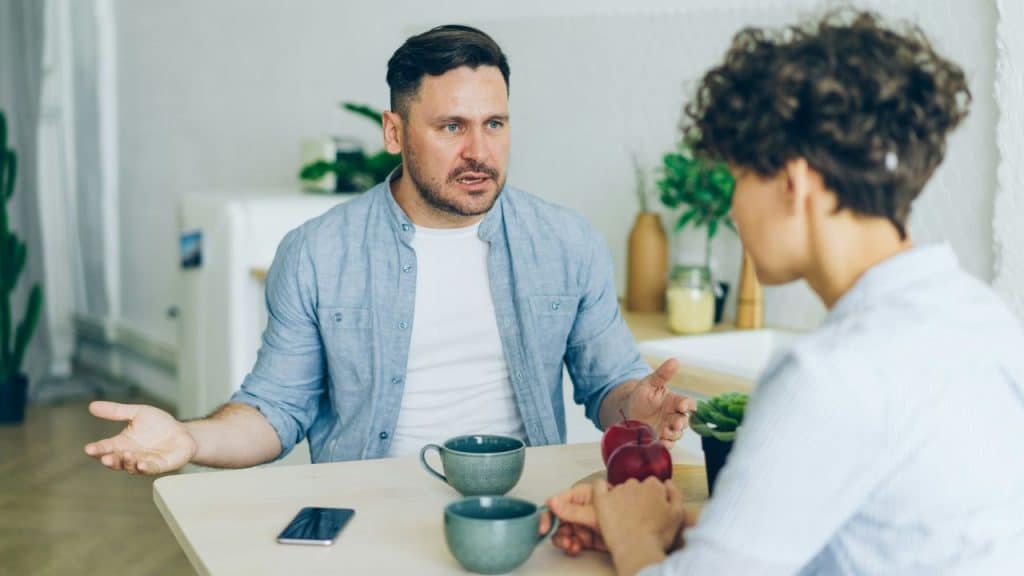 A man talks with expressive hands across a table from a woman in a casual setting.