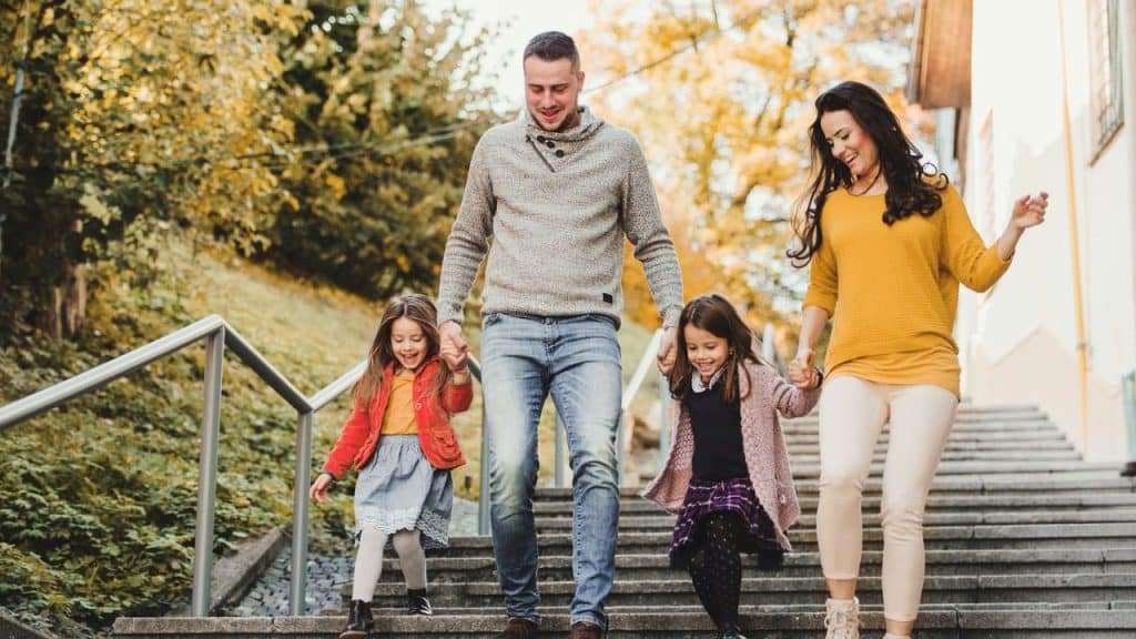 A family of four, including two young girls, walks down outdoor stairs in autumn.