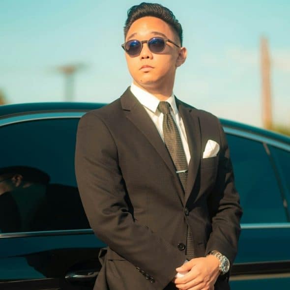 A man in a black suit standing beside a black car during daytime.
