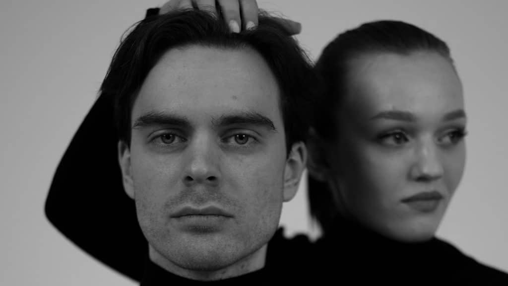 A man and woman pose in black turtlenecks.