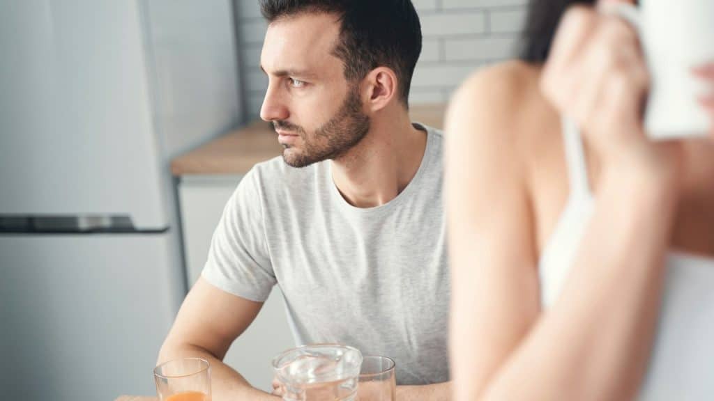A thoughtful man is sitting in the kitchen and is looking away.