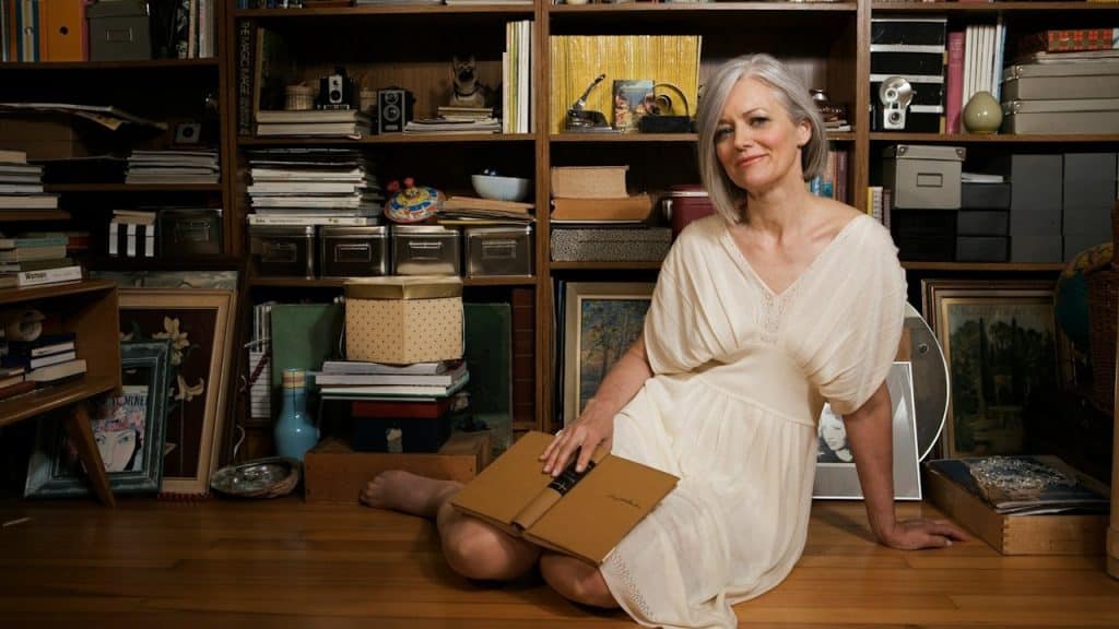 A woman sitting on the floor in front of a bookshelf.