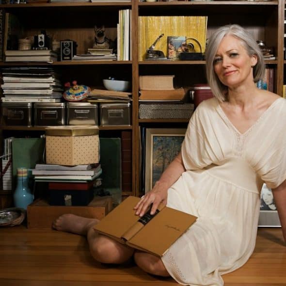 A woman sitting on the floor in front of a bookshelf.