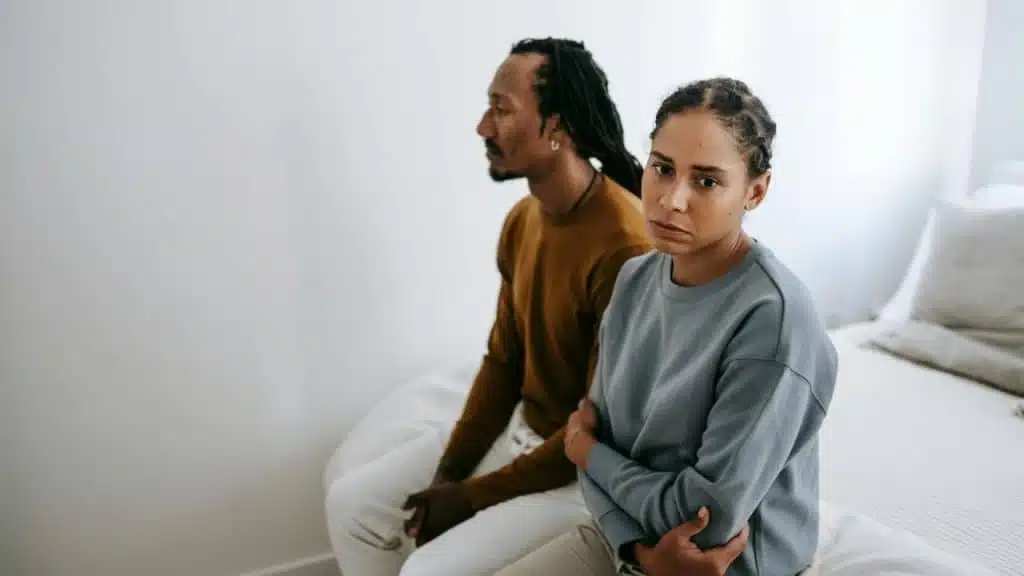 A woman with crossed arms looking unhappy while a man sits beside her looking away.