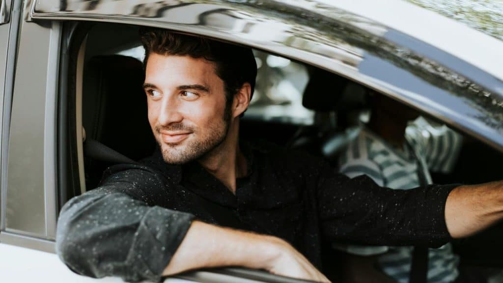 A man smiling while sitting in the driver’s seat of a car with the window open.
