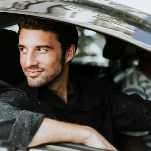 A man smiling while sitting in the driver’s seat of a car with the window open.