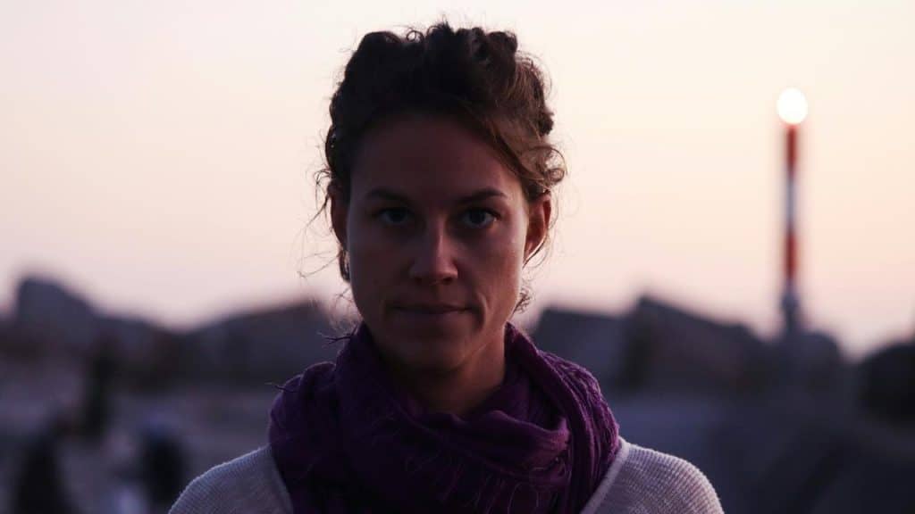 A woman standing outdoors at dusk with a calm, focused expression.